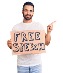 Young hispanic man holding free speech banner smiling happy pointing with hand and finger to the side
