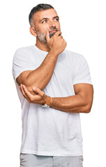 Middle age handsome man wearing casual white tshirt with hand on chin thinking about question,...