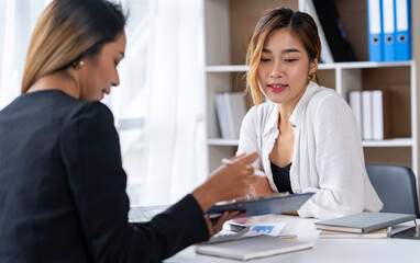 Two young businesswomen pointing to plans, statistics, and data graphs and explaining the conditions of their partnership, happily acknowledging their turnover and income during negotiations.