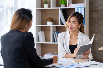 Two young Asian businessmen talk and discuss financial information. and the details planned by happily jotting down notes in a book...