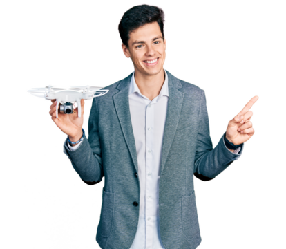 Young hispanic business man holding drone smiling happy pointing with hand and finger to the side