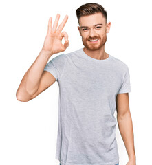 Fototapeta premium Young redhead man wearing casual grey t shirt smiling positive doing ok sign with hand and fingers. successful expression.