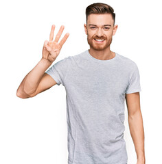 Young redhead man wearing casual grey t shirt showing and pointing up with fingers number three...