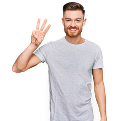 Naklejka premium Young redhead man wearing casual grey t shirt showing and pointing up with fingers number three while smiling confident and happy.