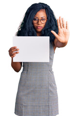 Beautiful african american woman holding blank empty banner with open hand doing stop sign with serious and confident expression, defense gesture