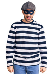 Young handsome man wearing burglar mask winking looking at the camera with sexy expression, cheerful and happy face.