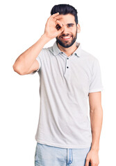 Fototapeta premium Young handsome man with beard wearing casual polo doing ok gesture with hand smiling, eye looking through fingers with happy face.