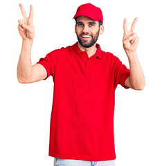 Fototapeta na wymiar Young handsome man with beard wearing delivery uniform smiling with tongue out showing fingers of both hands doing victory sign. number two.