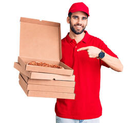 Young handsome man with beard wearing delivery uniform holding boxes with pizza smiling happy...