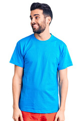 Young handsome man with beard wearing casual t-shirt looking away to side with smile on face, natural expression. laughing confident.