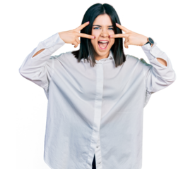 Young brunette woman with blue eyes wearing oversize white shirt doing peace symbol with fingers over face, smiling cheerful showing victory