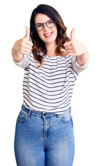Obraz na płótnie Canvas Beautiful young brunette woman wearing casual clothes and glasses approving doing positive gesture with hand, thumbs up smiling and happy for success. winner gesture.
