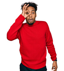 Young african american man with beard wearing casual winter sweater doing ok gesture shocked with surprised face, eye looking through fingers. unbelieving expression.