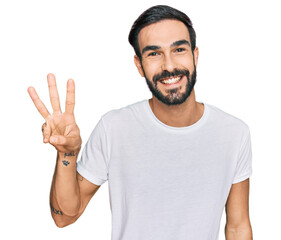 Fototapeta premium Young hispanic man wearing casual white t shirt showing and pointing up with fingers number three while smiling confident and happy.