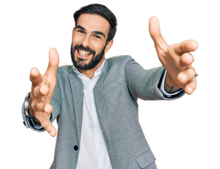 Young hispanic man wearing business clothes looking at the camera smiling with open arms for hug. cheerful expression embracing happiness. - obrazy, fototapety, plakaty