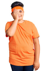Little boy kid wearing sportswear covering one eye with hand, confident smile on face and surprise emotion.