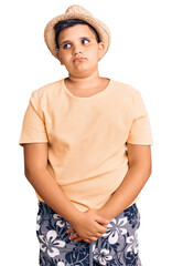 Little boy kid wearing summer hat and hawaiian swimsuit smiling looking to the side and staring away thinking.