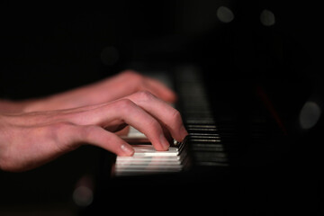 A close up of a pianists hands and fingers playing the keys on a piano. Isolated against a...