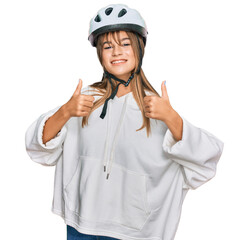 Teenager caucasian girl wearing bike helmet success sign doing positive gesture with hand, thumbs up smiling and happy. cheerful expression and winner gesture.