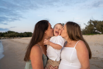 lesbian moms kissing son on cheek on beach