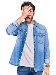 Young hispanic man wearing casual clothes peeking in shock covering face and eyes with hand, looking through fingers with embarrassed expression.