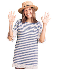Obraz na płótnie Canvas Beautiful caucasian woman wearing summer hat showing and pointing up with fingers number ten while smiling confident and happy.