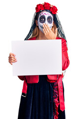 Woman wearing day of the dead costume holding blank empty banner covering mouth with hand, shocked and afraid for mistake. surprised expression