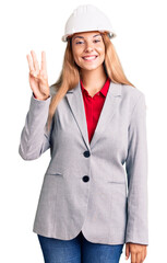 Beautiful young woman wearing architect hardhat showing and pointing up with fingers number three while smiling confident and happy.