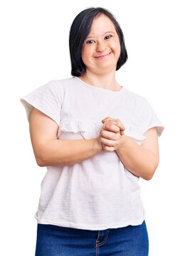 Brunette woman with down syndrome wearing casual white tshirt with hands together and crossed fingers smiling relaxed and cheerful. success and optimistic