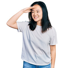 Fototapeta premium Young chinese woman wearing casual white t shirt very happy and smiling looking far away with hand over head. searching concept.