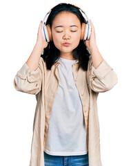 Young chinese woman listening to music using headphones looking at the camera blowing a kiss being lovely and sexy. love expression.