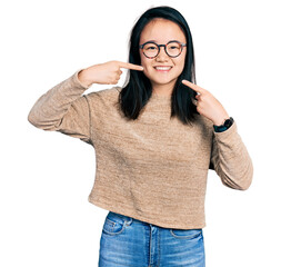 Young chinese woman wearing casual sweater and glasses smiling cheerful showing and pointing with fingers teeth and mouth. dental health concept.