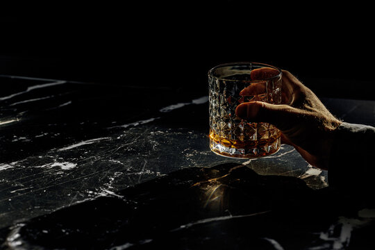 Hand Holding A Whiskey Glass In A Marble Table