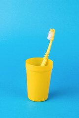 A yellow glass with a yellow toothbrush on a light blue background.