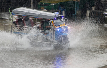 A traditional motorized tricycle - tuk tuk drives through a puddle on the road in heavy rain,...