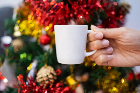 Blur image of hand holding a white cup with christmas tree background. Background image