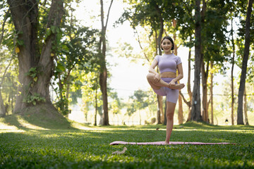 Attractive young Asian woman practice yoga, exercise in the park, standing one leg on a yoga mat, showing balance posture. Wellbeing lifestyle and activity concept