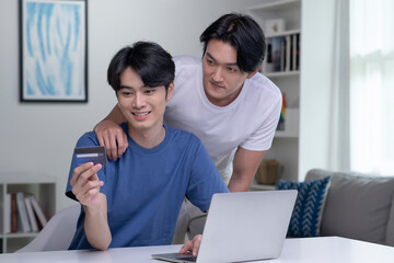 Young Asian gay couple holding credit card and using laptop computer. LGBT gay businessman working at home. Online shopping, e-commerce, internet banking, spending money, working from home concept