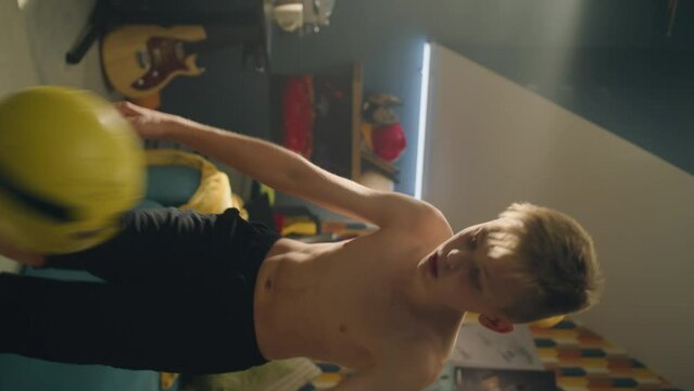 Vertical video shot of young football player performs tricks with his knees and controlling the soccer ball. Shirtless young boy do sports. Football fan. School sports team player.