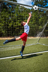 Youth male soccer player goalie jumping to catch the ball