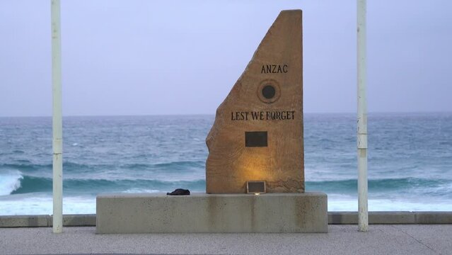 Close up to ANZ war memorial cenotaph carved with Lest We Forget with rapid and vigorous wave crashing on to the shore in the background at surfers paradise, Gold Coast, Queensland, Australia.