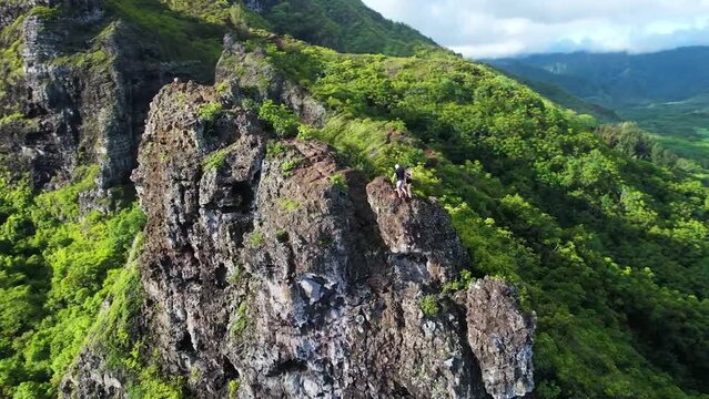 Aerial Orbit of Two Hikers on Edge of Rocky Cliff in Tropical Hawaii