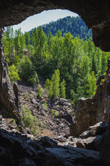 Obraz premium View from the stone cave outside to the coniferous forest. Beautiful summer landscape in good weather.