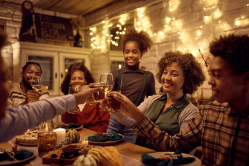 Happy black extended family toasting and having fun while gathering for Thanksgiving meal at dining table.
