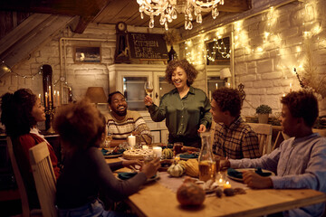 Happy black mature woman holding a toasting during family dinner on Thanksgiving.
