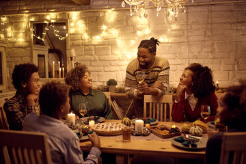 Happy African American man holding toasting during dinner with his extended family on Thanksgiving.