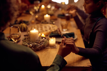 Close up of black family holding hands while saying grace during Thanksgiving meal.