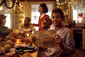 Smiling black boy with Happy Thanksgiving message during family dinner at dining table.