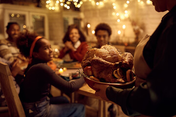 Close up of black woman celebrating Thanksgiving with her family and serving them roast turkey for dinner.