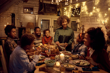 Happy black grandmother serving food during family lunch on Thanksgiving.